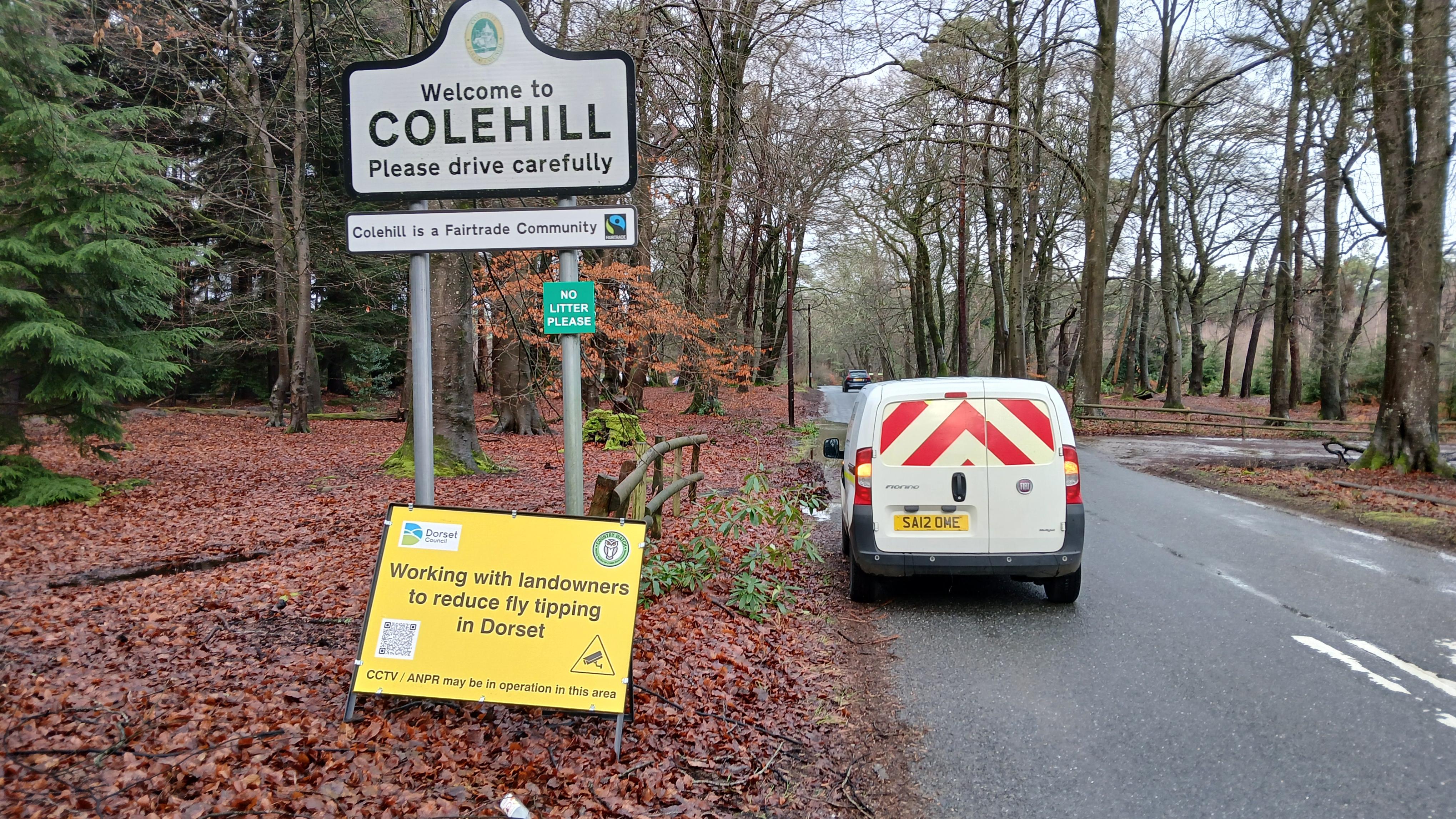 A van is parked on the side of a road next to a sign that says Welcome to Colehill Please drive carefully. There is also a temporary yellow sign that says working with landowners to reduce fly tipping in Dorset.