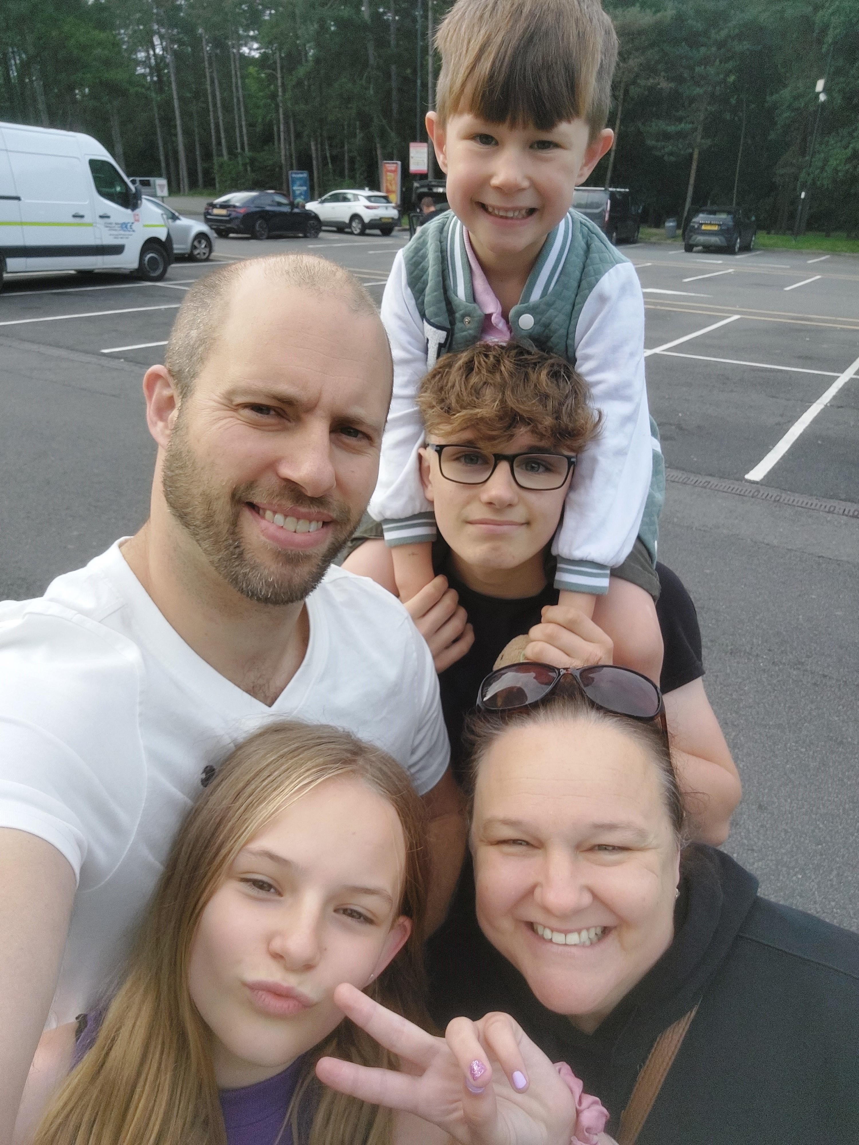 A man and woman smile at the camera, alongside their 3 children.