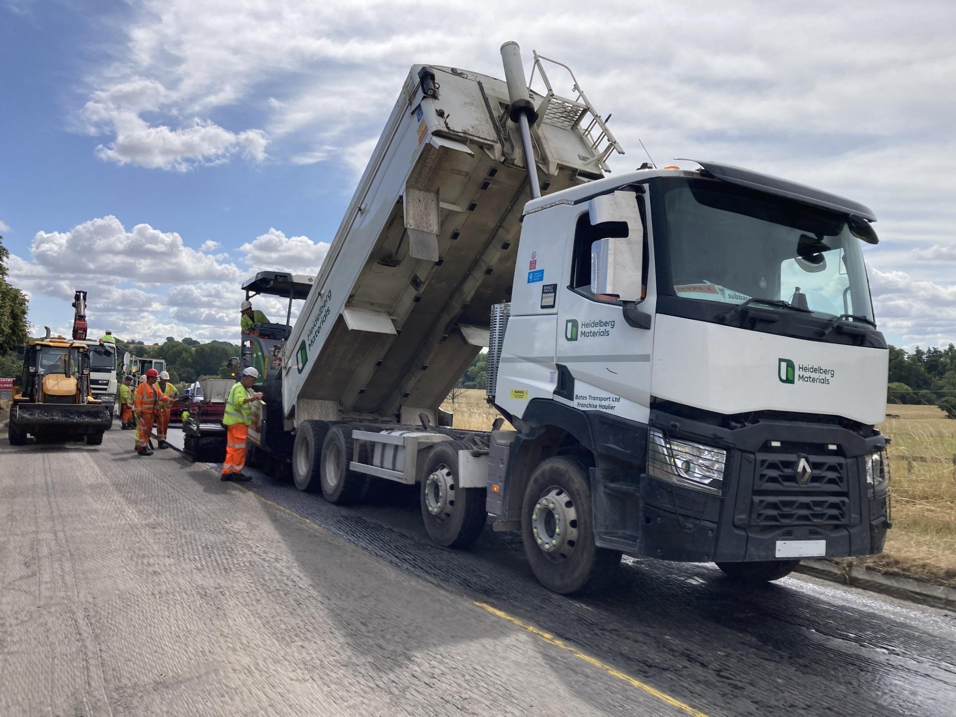 A large white lorry tilted to deliver unload surfacing materials on to the road