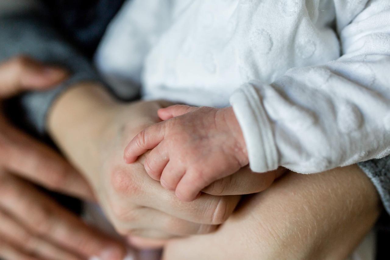 the photo is a close up of a mother and father holding their baby's hand.