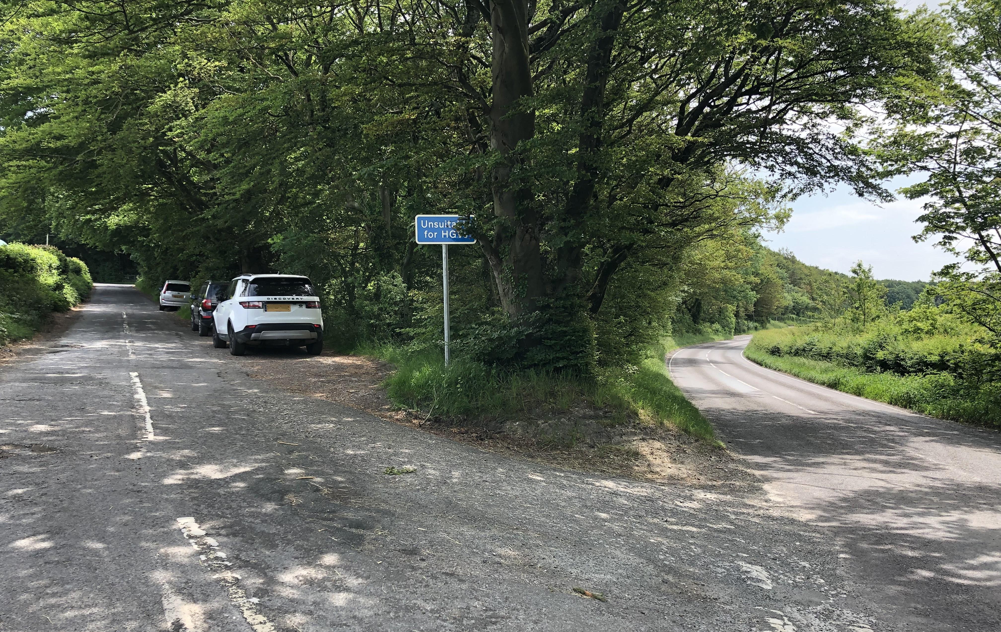 A turning of a main road with a white car, a black car and a silver car parked on the right