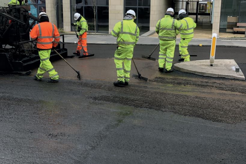 Highways works in yellow and orange high visibility clothing sweeping a road surface