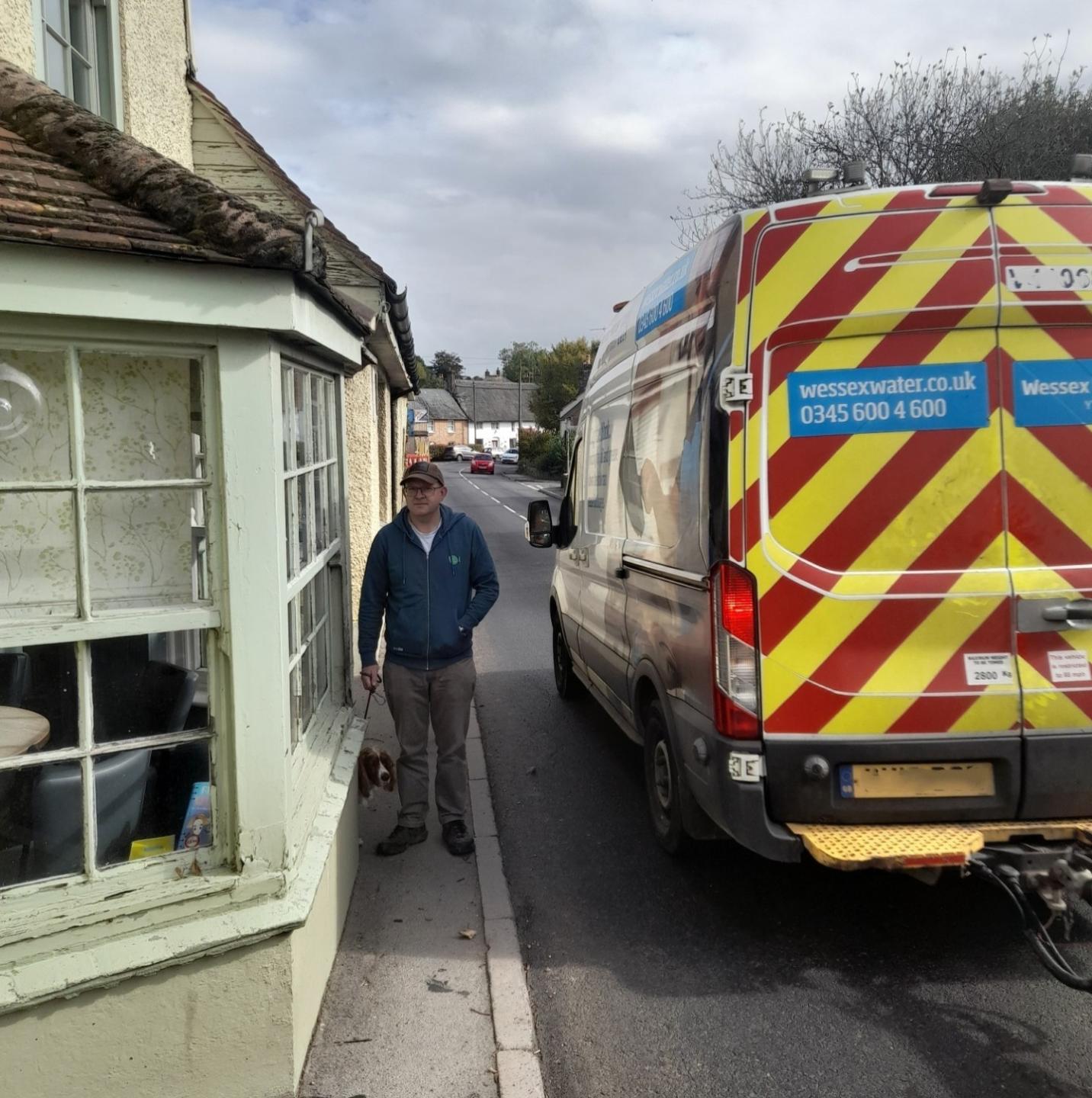 A man and his dog squeezing onto a narrow pavement as a large vehicle passes them