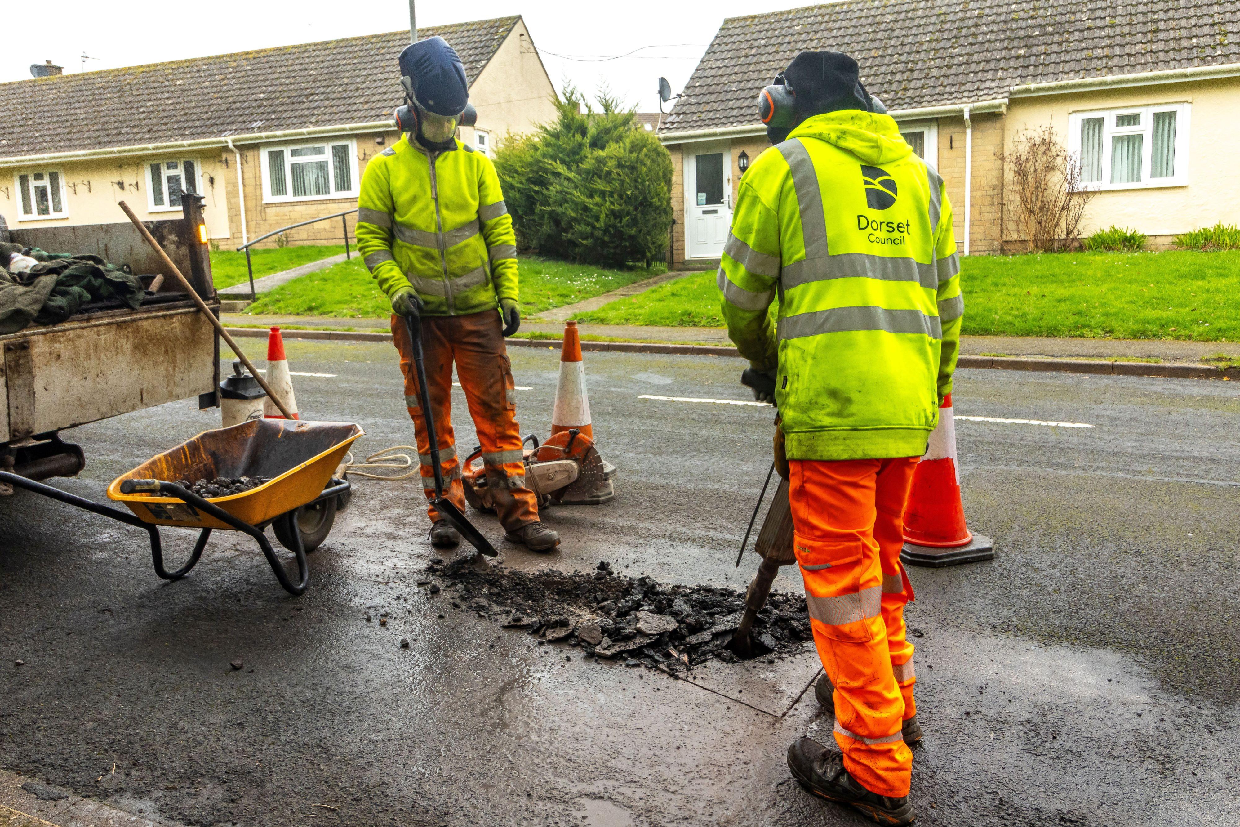 Two workmen wearing yellow jackets and orange trousers repairing a pothole