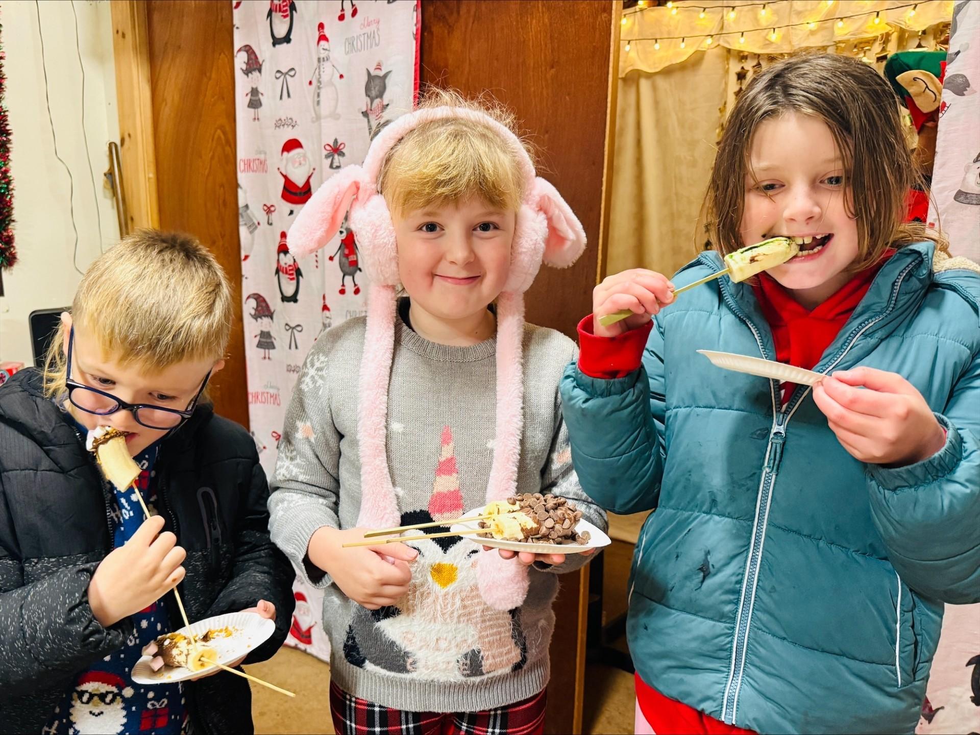 Three children in winter coats enjoying food