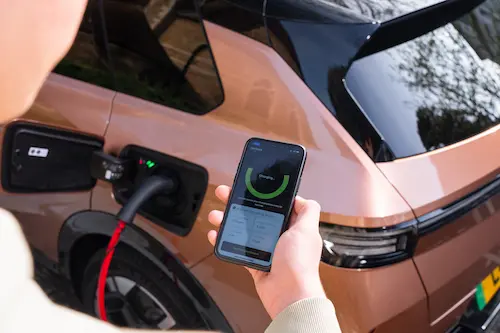 Person holding a smartphone to check an EV’s charging status while the car is plugged in