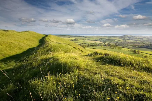 Rolling green hills and open countryside under a partly cloudy sky.