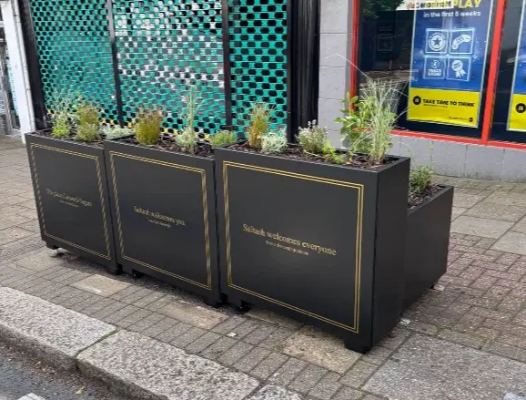 Rear view of a heritage‑style planter with integrated bench unit, showing black rectangular planters with gold detailing and planted greenery.