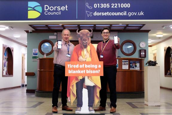 two men stand either side of bison cut out holding their phones in front of them