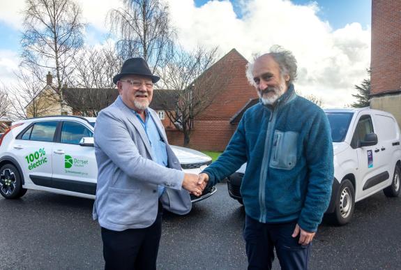 Two men shaking hands in front of an EV car with the Dorset Council logo on it and an EV van with the BCP Council logo on it