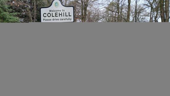A van is parked on the side of a road next to a sign that says Welcome to Colehill Please drive carefully. There is also a temporary yellow sign that says working with landowners to reduce fly tipping in Dorset.