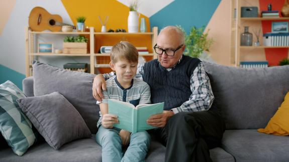Older man reading to a child, sat on a couch with a book